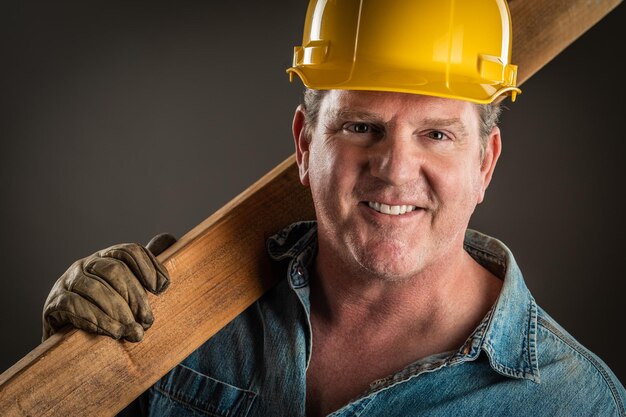 Foto glimlachende aannemer in een harde hoed met een houten plank met dramatische verlichting