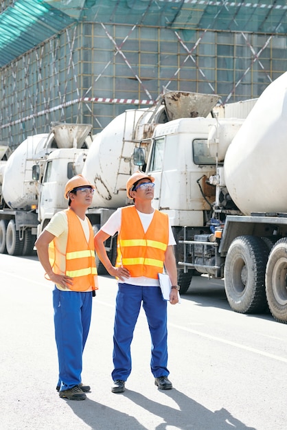 Glimlachende aannemers die langs rijen betonmixers lopen en een werkdag plannen bij de bouw...