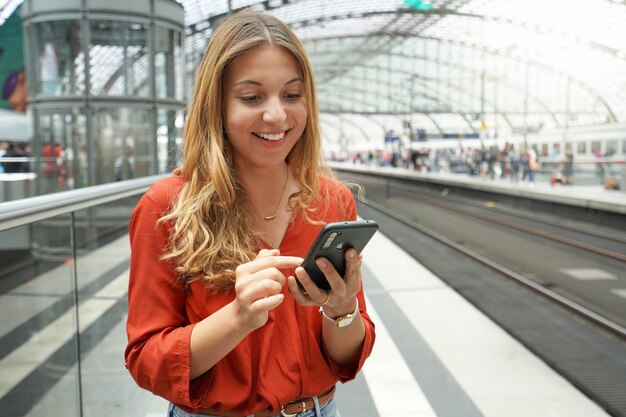 Glimlachende aantrekkelijke Braziliaanse reiziger passagier koopt online ticket met smartphone in treinstation Ruimte kopiëren