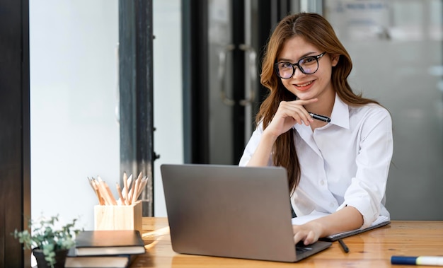 Glimlachende aantrekkelijke vrouw die met glazen aan laptop computer op kantoor werken die aan camera kijken