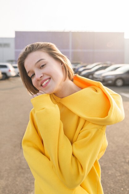 Glimlachende aantrekkelijke vrouw in een gele hoodie die zich in de straat bevindt