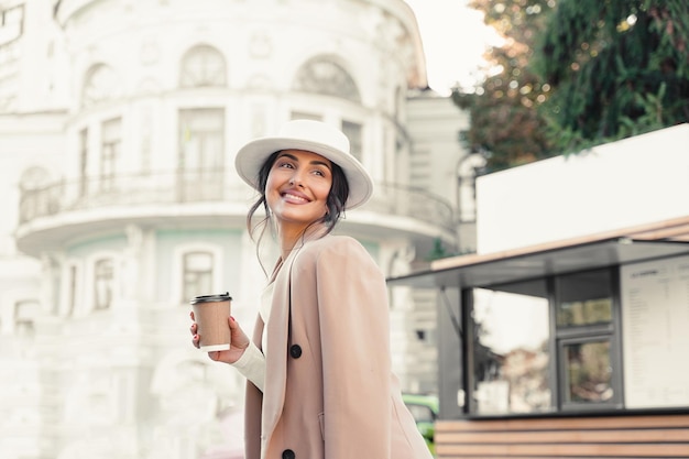 Glimlachende aantrekkelijke vrouw met kopje koffie in de buurt van coffeeshop. Zakelijke dame heeft een pauze.