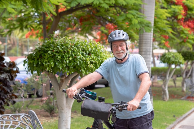 Glimlachende actieve senior man fietsen in het openbare park met elektrische fiets genieten van vrijheid Concept van gezonde levensstijl en duurzame mobiliteit