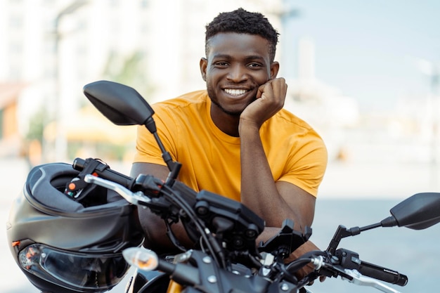 Glimlachende Afrikaans-Amerikaanse man motorrijder met helm en kijkt naar de camera in de buurt van sport motorfiets