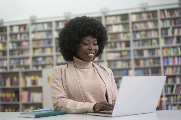 Glimlachende Afrikaanse student die een laptopcomputer gebruikt die studeert in een modern bibliotheekonderwijsconcept