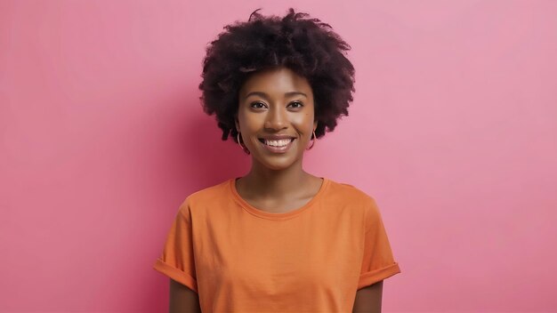 Glimlachende Afrikaanse vrouw die naar de camera kijkt met een casual oranje t-shirt geïsoleerd op roze