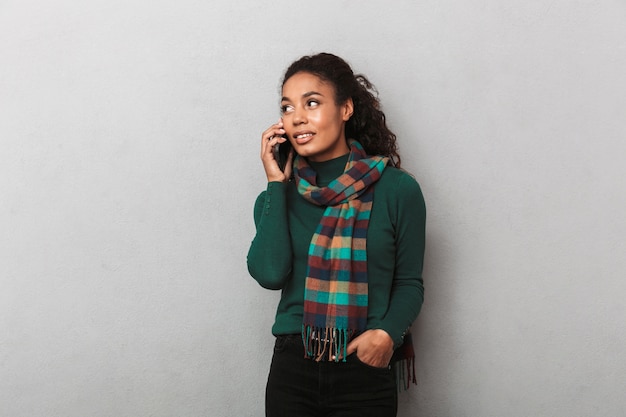 Glimlachende Afrikaanse vrouw die vacht draagt die, mobiele telefoon gebruikt