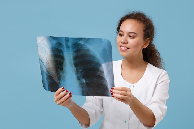 Glimlachende afro-amerikaanse dokter vrouw in witte medische jurk houdt röntgenfoto van longen, fluorografie, röntgen geïsoleerd op blauwe achtergrond. gezondheidszorg personeel geneeskunde gezondheid concept. mock up kopie ruimte.
