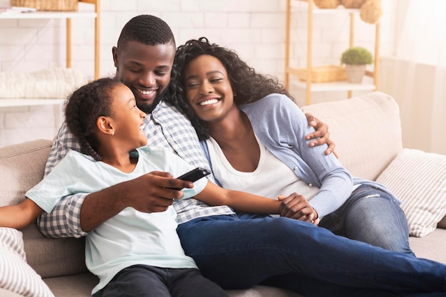 Glimlachende Afro-Amerikaanse familie ontspannen op de bank en thuis tv kijken, man schakelen tussen kanalen