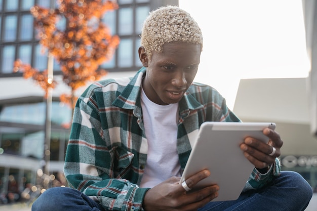 Glimlachende afro-amerikaanse student met behulp van digitale tablet studeren, taal leren zittend op de campus