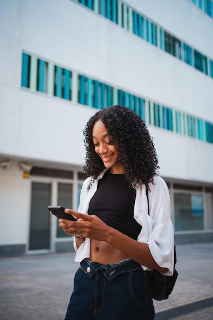 Glimlachende Afro-Amerikaanse vrouw die een sms naar haar vrienden stuurt terwijl ze in de stad is