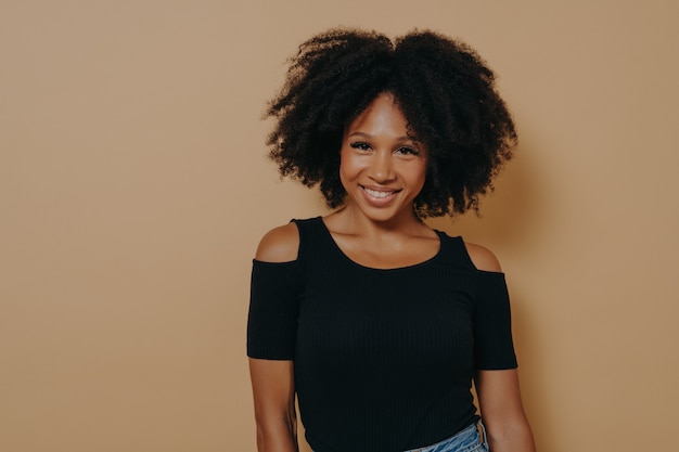 Glimlachende afro-amerikaanse vrouw met krullend haar die zich tegen beige achtergrond bevinden
