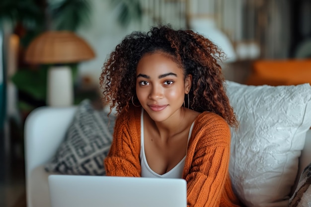 glimlachende Afro-Amerikaanse vrouw zit op de bank met behulp van een laptop externe werk of studie concept