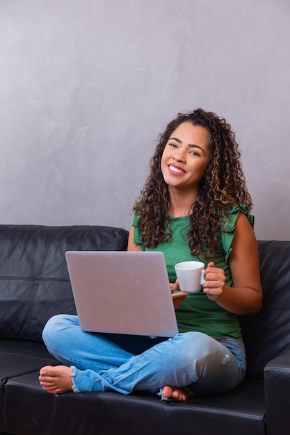 Glimlachende afro jonge vrouw met behulp van laptop, zittend op de bank thuis, mooi meisje winkelen of online chatten in sociaal netwerk, plezier hebben, film kijken, freelancer werken aan computerproject