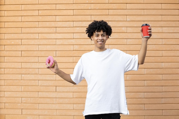 Glimlachende Amerikaanse man met een kopje koffie en een roze donut aan de zijkanten in een wit T-shirt