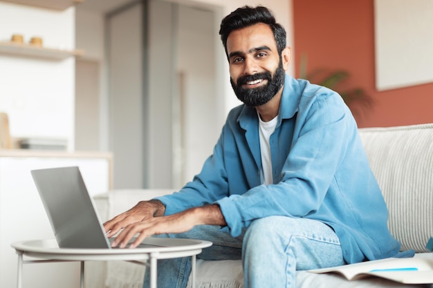 Glimlachende arabische man die aan laptop werkt die in de woonkamer zit