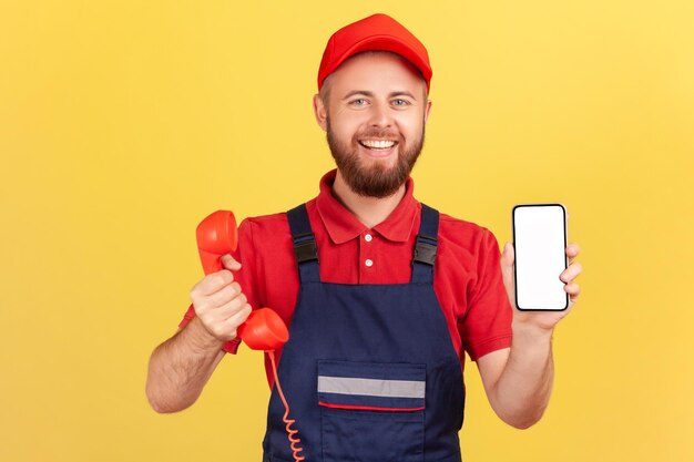 Glimlachende arbeidersmens die retro telefoon en celtelefoon met leeg scherm voor reclame standhoudt