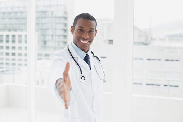 Glimlachende arts die een handdruk in een medisch bureau aanbieden