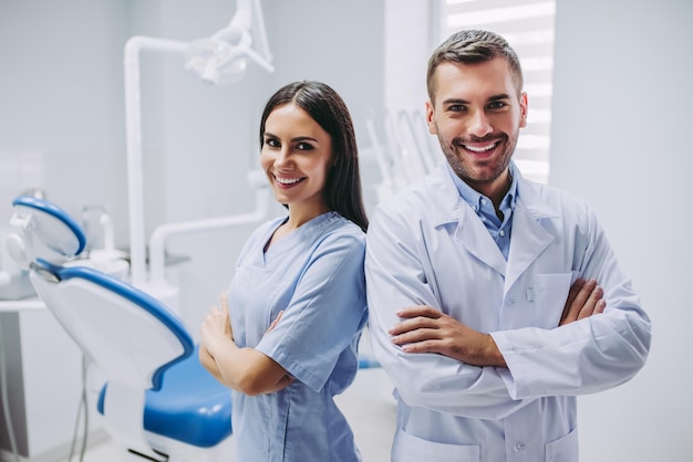 Foto glimlachende arts en assistent met gekruiste handen kijken naar de camera in de tandheelkundige kliniek