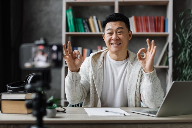 Glimlachende aziatische man die videoblog opneemt en duim laat zien