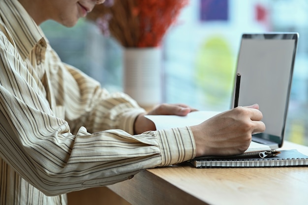 Glimlachende Aziatische man met behulp van laptop en het maken van aantekeningen op Kladblok.