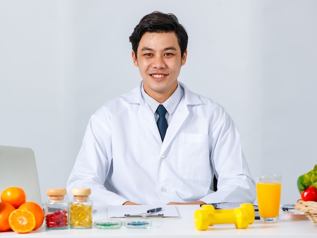 Glimlachende Aziatische mannelijke voedingsdeskundige die aan tafel zit met diverse vers fruit en naar de camera kijkt terwijl hij het concept van gezonde voeding laat zien