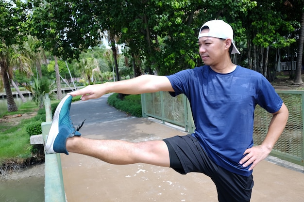 Glimlachende Aziatische sportman die zijn been traint en strekt voor spierontspanning en veerkrachtig na hardlopen en joggen in de tuin.