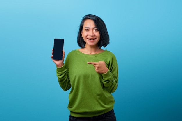 Glimlachende Aziatische vrouw die een leeg smartphonescherm toont en erop wijst terwijl ze naar de camera kijkt