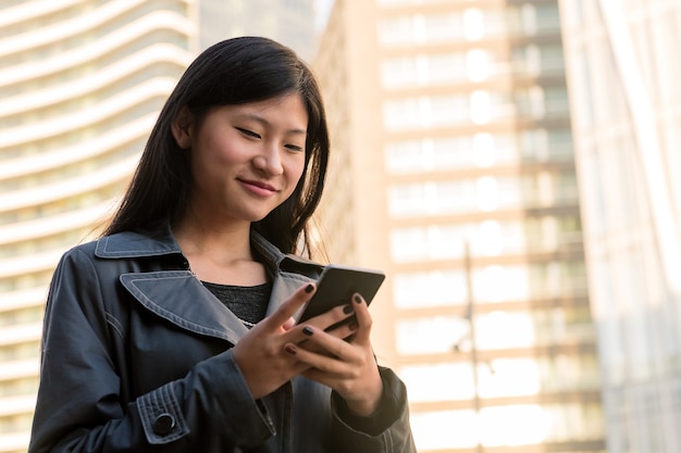 Glimlachende Aziatische vrouw die haar mobiele telefoon raadpleegt