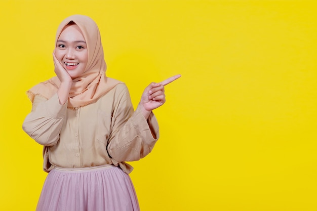Glimlachende Aziatische vrouw die hijab draagt met haar vinger wijzend geïsoleerd op lichtgele bannerachtergrond