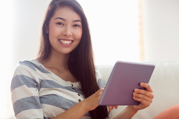 Glimlachende Aziatische vrouw die tablet op laag gebruiken