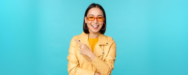 Glimlachende aziatische vrouw in zonnebril die met de vinger naar links wijst en bannerlogo of advertentie op een blauwe achtergrond toont
