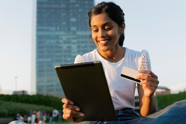 Glimlachende Aziatische vrouw met behulp van digitale tablet met creditcard online winkelen buiten zitten