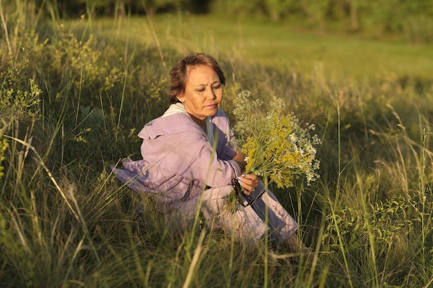 Glimlachende Aziatische vrouw van oudere leeftijd in een zomerpark met wilde bloemen, de video brengt een