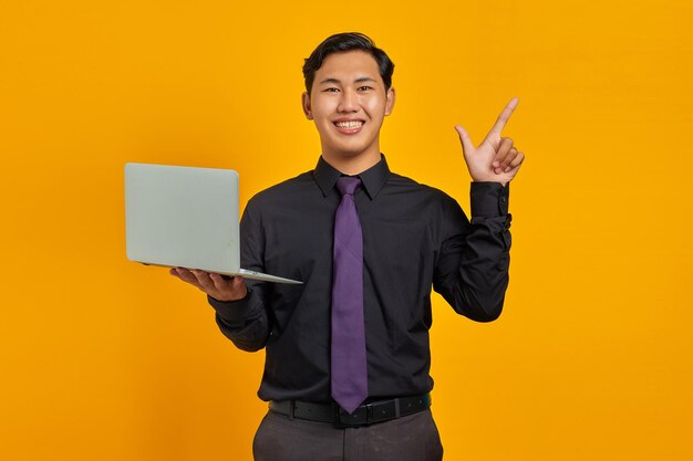 Glimlachende Aziatische zakenman met creditcard wijzende vinger naar kopieerruimte op gele achtergrond