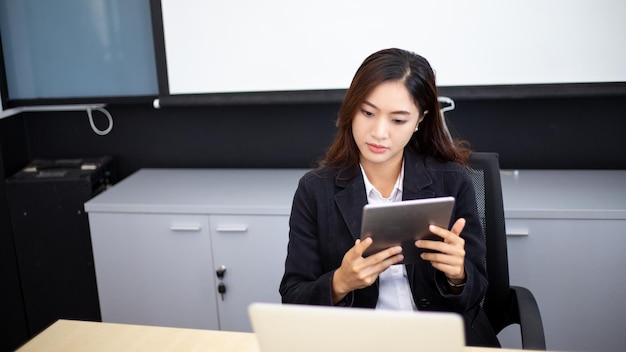 Glimlachende Aziatische zakenvrouw die tablet gebruikt voor werk en schattig meisje dat op zoek is naar wat gegevens en zich concentreert op haar tablet in haar kantoor