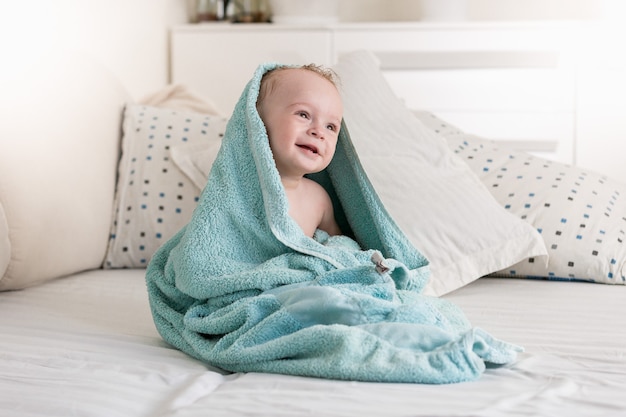 Glimlachende baby bedekt met blauwe handdoek na het baden