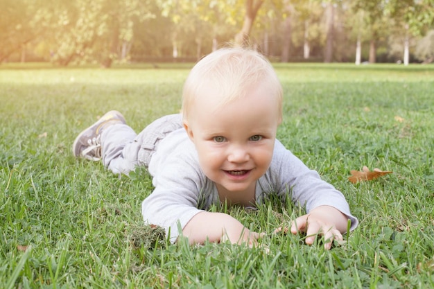 Glimlachende babyjongen die buiten op het groene gras ligt
