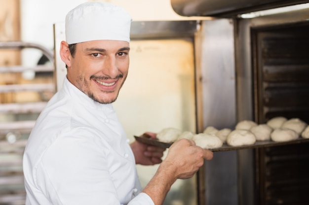 Glimlachende bakker die deeg in oven zet