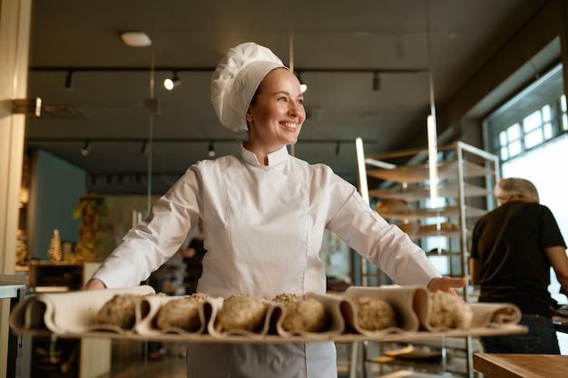 Glimlachende bakker die zoete broodjesgebakjes met sesamzaden voorbereidt