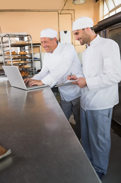 Glimlachende bakkers die aan laptop samenwerken