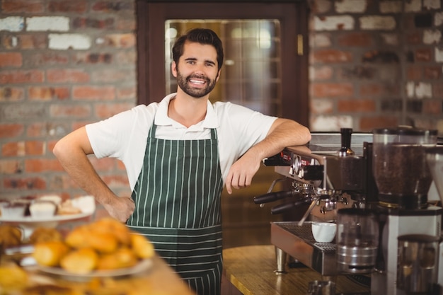 Glimlachende barista die op de koffiemachine leunt