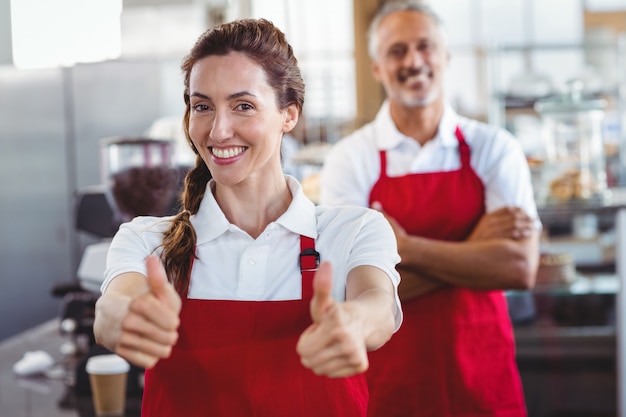 Glimlachende barista gesturing duimen omhoog met erachter collega