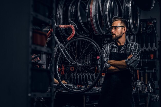 Glimlachende bebaarde man met bril staat in de buurt van een vaste fiets in zijn eigen werkplaats.