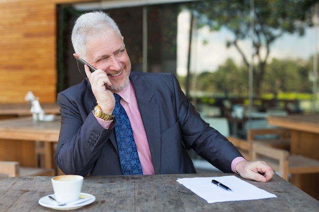 Glimlachende bedrijfsmens die op Smartphone in Koffie spreekt