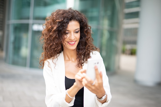 Glimlachende bedrijfsvrouw die haar mobiele celtelefoon met behulp van terwijl in openlucht het lopen