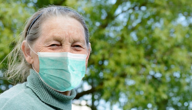 Glimlachende bejaarde dorpsgrootmoeder die in openlucht medisch beschermend masker draagt. Preventie tijdens Coronavirus COVID-19 pandemie