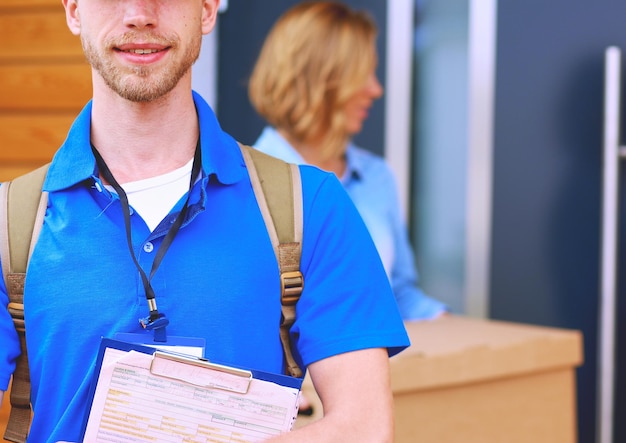 Glimlachende bezorger in blauw uniform die pakketdoos levert aan ontvanger koeriersdienstconcept smil