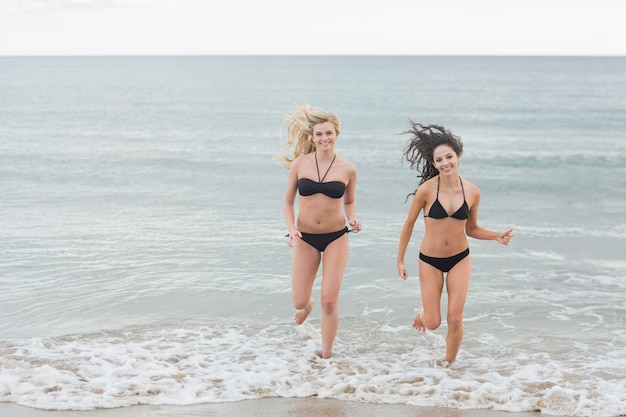 Glimlachende bikinivrouwen die in water bij strand lopen