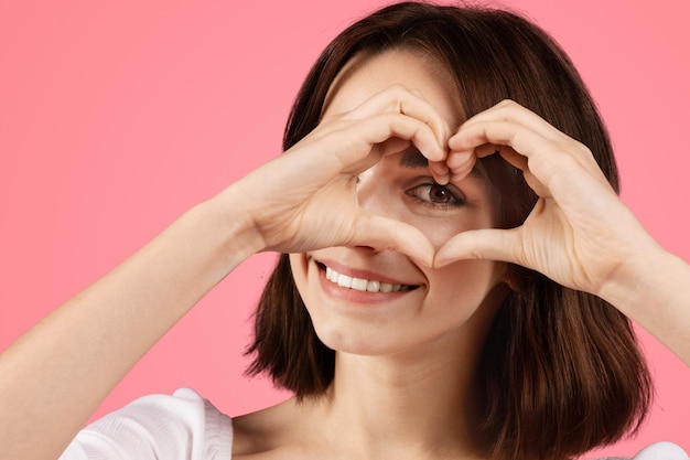 Glimlachende blanke brunette vrouw die hart gebaar maakt met haar handen.